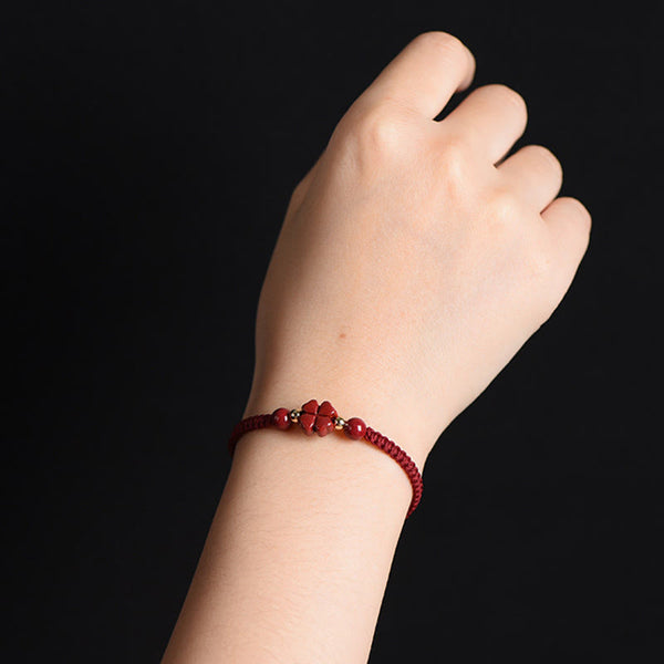 Burgundy braided cord bracelet with carved four-leaf clover charm and gold spacer beads worn on wrist against solid black background
