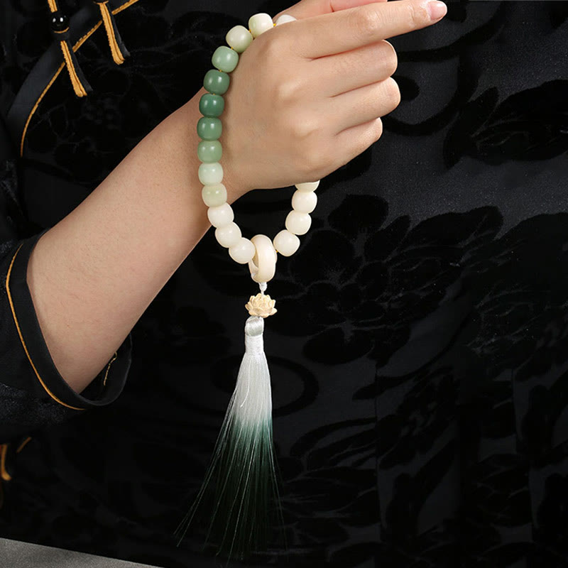Bodhi Seed Lotus Wisdom Wrist Mala – Green gradient bracelet on wrist with black Tang suit, gold piping and lotus tassel, cultural jewelry