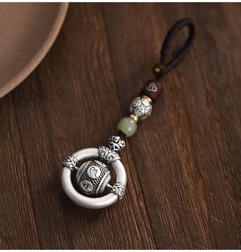 Mantra Keychain – silver spinning prayer bead in ring on brown cord, wooden table with ceramic bowl