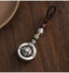 Mantra Keychain – silver spinning prayer bead in ring on brown cord, wooden table with ceramic bowl