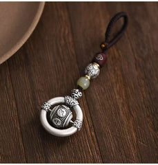 Mantra Keychain – silver spinning prayer bead in ring on brown cord, wooden table with ceramic bowl
