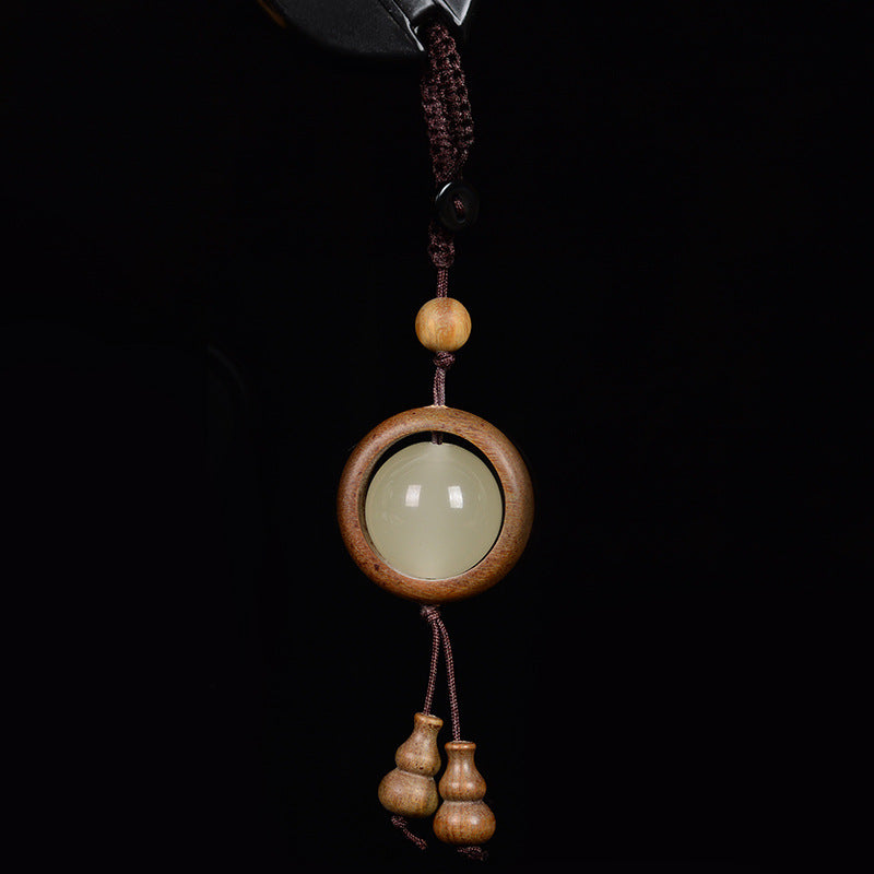 Feng Shui Sandalwood Keychain with Luminous Bead – Green sandalwood circular frame with glowing jade center and double gourd pendant on black background