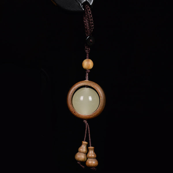 Feng Shui Sandalwood Keychain with Luminous Bead – Green sandalwood circular frame with glowing jade center and double gourd pendant on black background