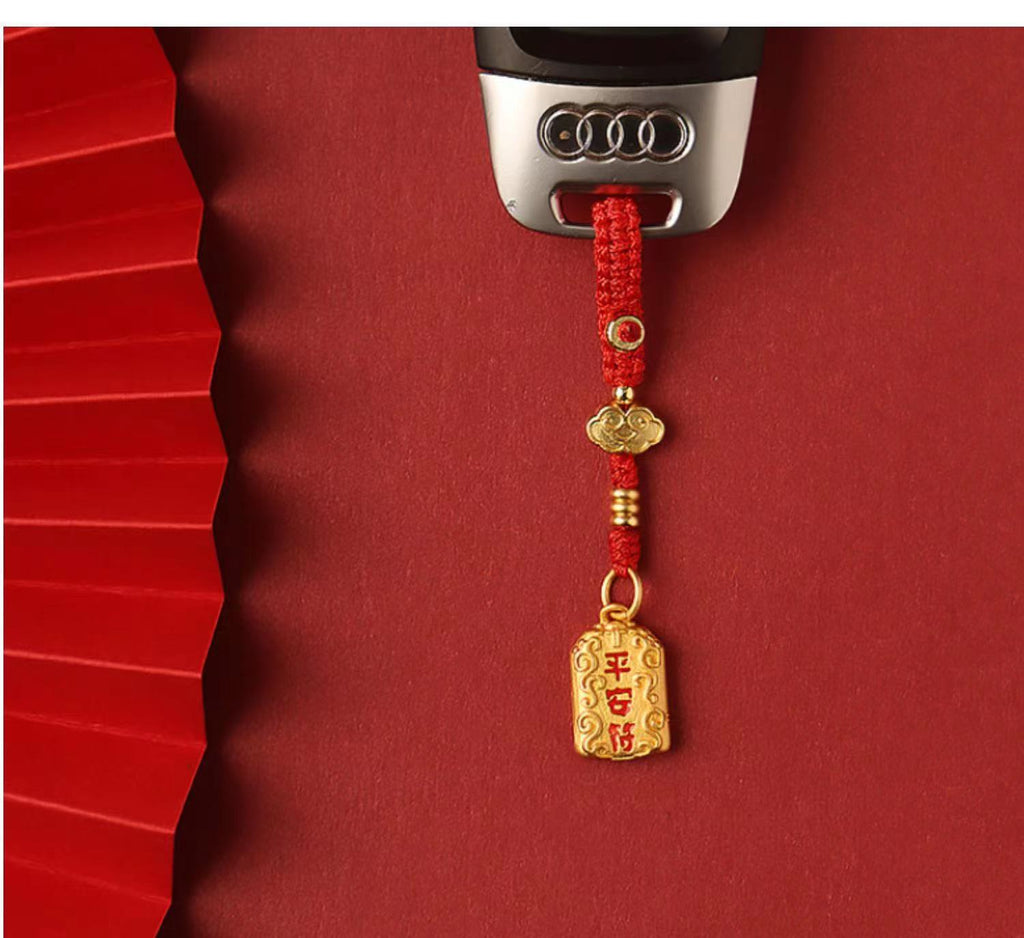 Brass peace charm keychain with red braided rope attached to car key, red background