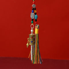 Tibetan Prayer Wheel Keychain – two-tone silver and gold prayer wheel pendant with colorful silk tassel, turquoise beads and auspicious knot charm, red background, front vertical view