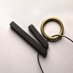 Zen Circle Ebony Wood Necklace - hammered bars with brass ring on off-white surface, minimalist artisan jewelry
