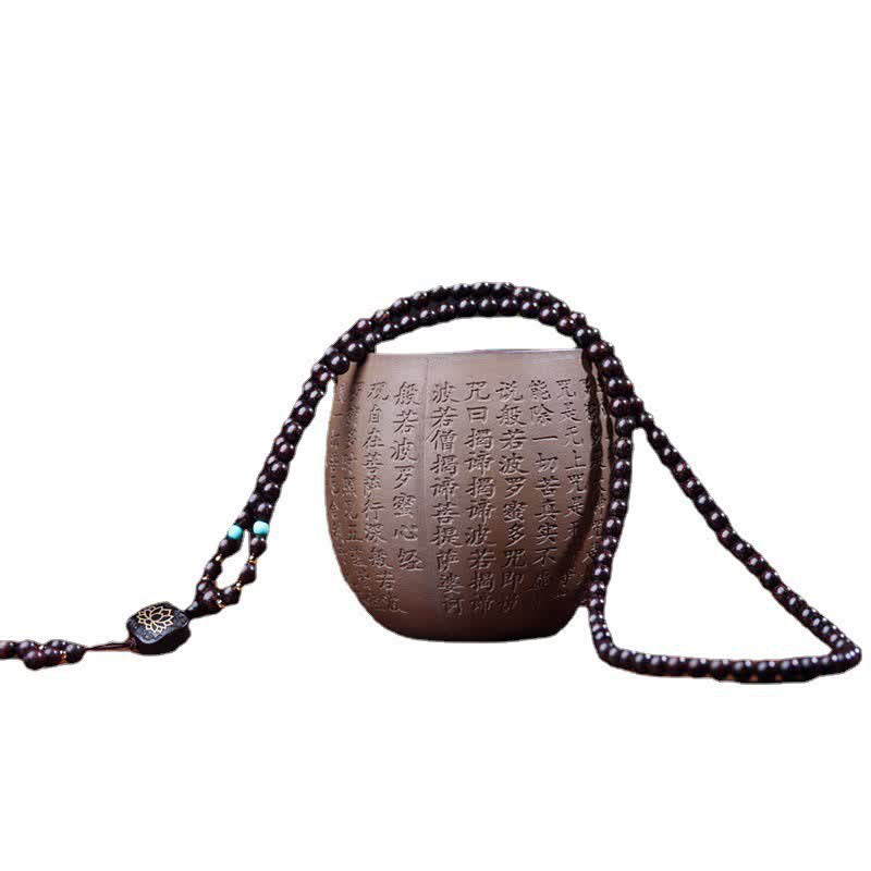 108 bead red sandalwood mala prayer beads artfully draped over ceramic vessel with Buddhist scripture calligraphy on white background with lotus guru bead pendant