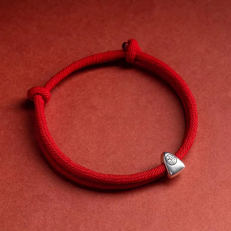 925 Silver Fu Character Braided Bracelet – Red braided cord bracelet with silver geometric accent bead on reddish-brown matte textured surface, low side angle