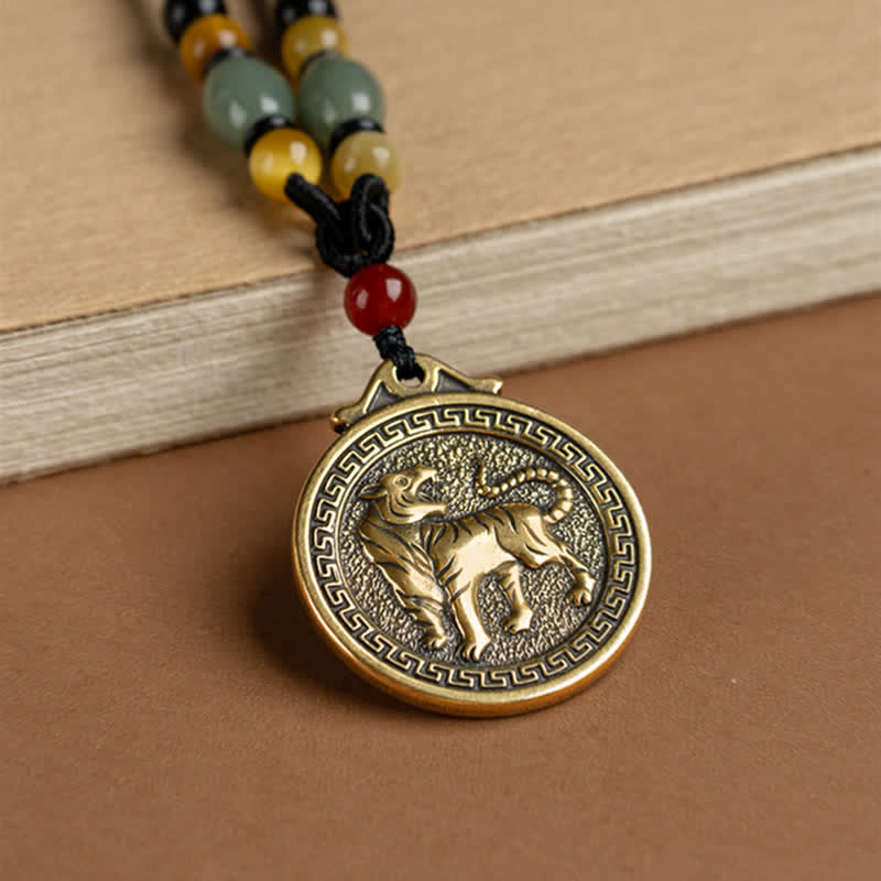 12 Chinese Zodiac Fortune Necklace Pendant – Tiger zodiac pendant on brown leather with aged book props, antique gold medallion with dynamic tiger relief, stippled metal texture, Greek key border, beaded cord with jade and carnelian, scholarly traditional aesthetic