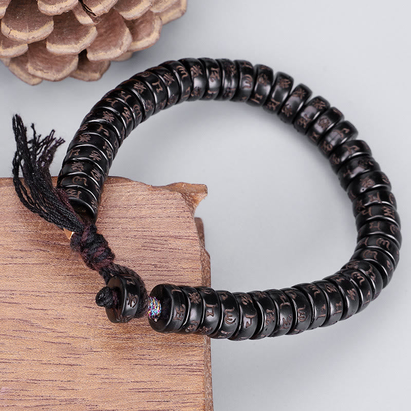 Coconut Shell Om Mani Padme Hum Bracelet – dark carved mantra disc beads on burgundy cord with tassel, pinecone and wood prop