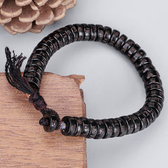 Coconut Shell Om Mani Padme Hum Bracelet – dark carved mantra disc beads on burgundy cord with tassel, pinecone and wood prop