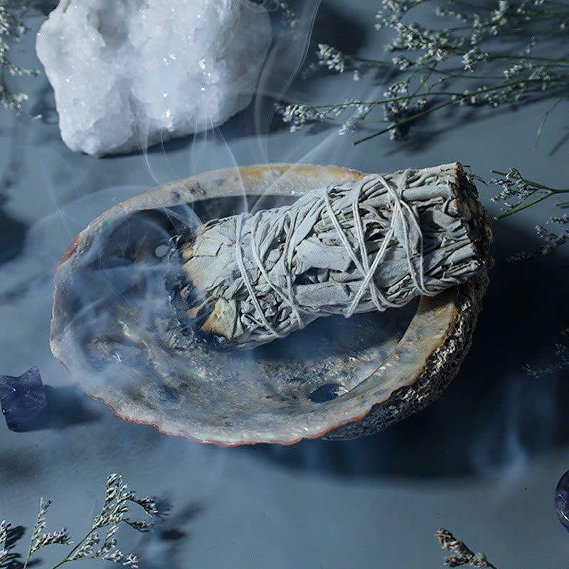 White sage smudge stick burning in abalone shell with quartz and amethyst
