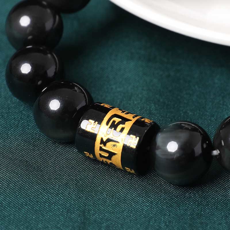 Rainbow Obsidian Bracelet – Macro detail of gold engraved mantra bead among glossy obsidian spheres, Buddhist bracelet