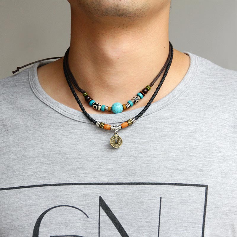 Turquoise Dzi Bead Protection Necklace – worn by male model on gray t-shirt showing double-strand design, turquoise focal bead on upper strand and antique brass coin pendant on lower strand, black braided leather cord with adjustable knot closure