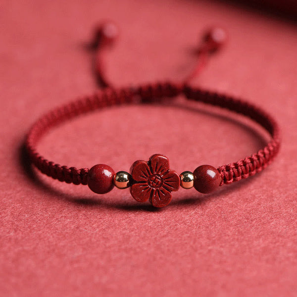 Adjustable red braided cord bracelet with carved cinnabar five-petal flower charm, gold-tone spacer beads and round red beads on textured red surface