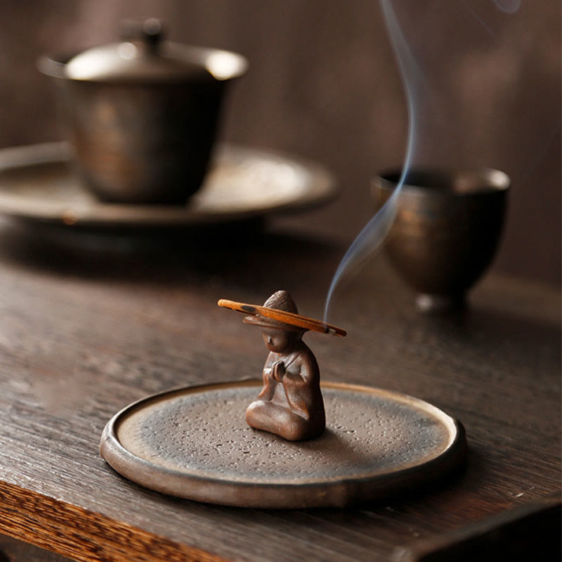 Terracotta meditating monk with lit incense stick on wood grain table, healing