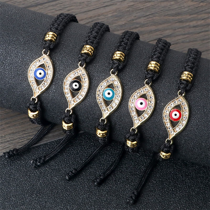 Five black cord evil eye bracelets with gold crystal charms on dark display stand