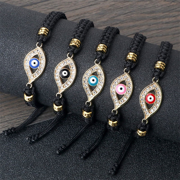 Five black cord evil eye bracelets with gold crystal charms on dark display stand
