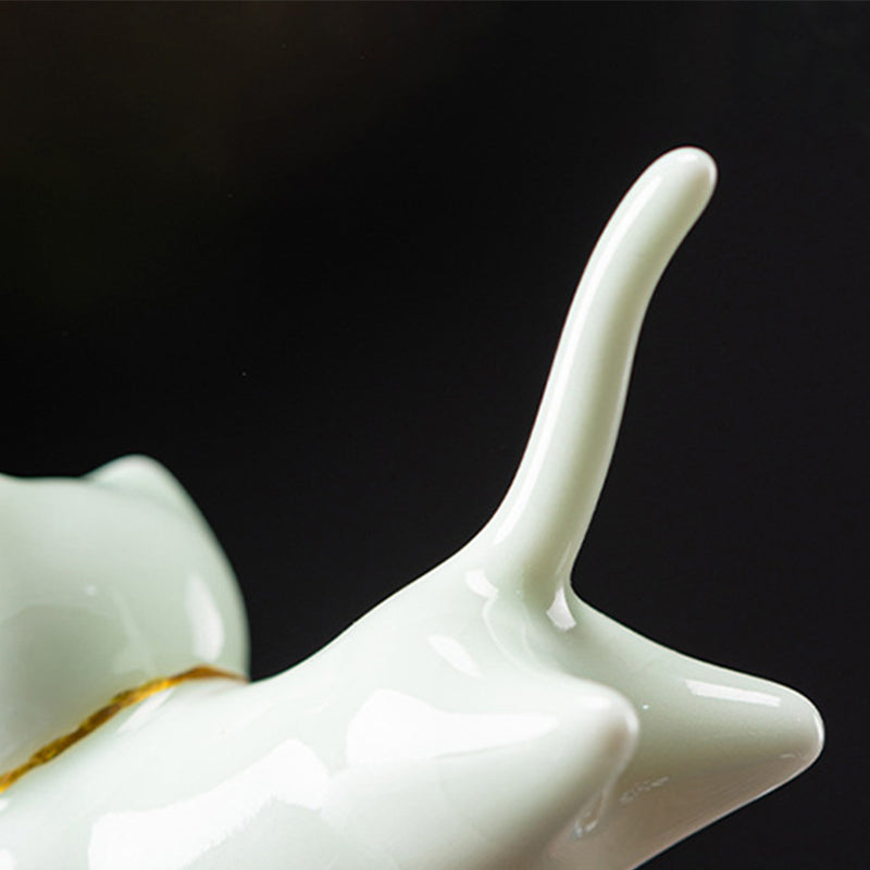 White ceramic cat figurine with gold accent band, curved tail, black backdrop