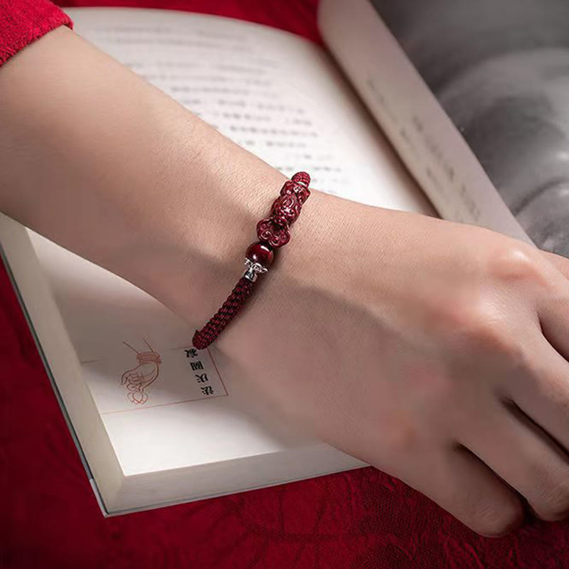 Handcrafted PiXiu Cinnabar Wealth Luck Braided Bracelet – worn on wrist over open book page, red sleeve elegant