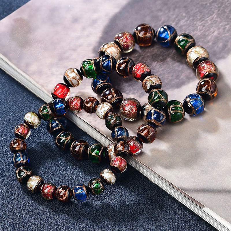 Colorful Liuli Glass Bead Luck Bracelet – Vibrant multicolored glass beads with pale blue center bead and gold spring-ring clasp on cream silk fabric, low angle