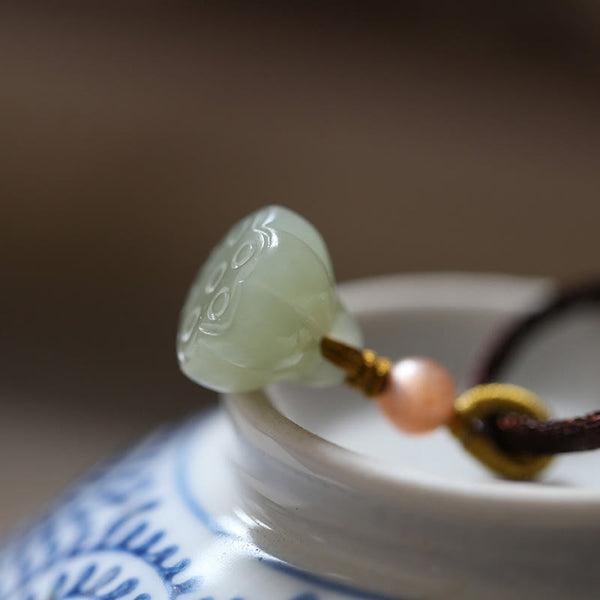 Jade Peace Buckle Lotus Necklace – Lotus seed pod jade pendant on brown cord on blue-and-white porcelain, lotus jade