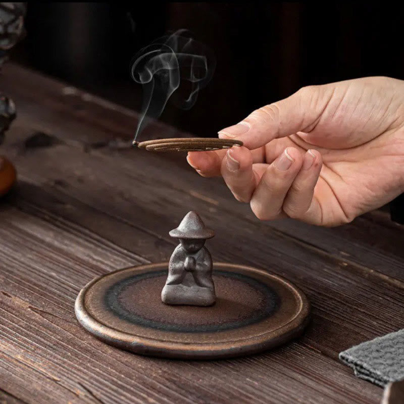 Dark monk figure receiving coil incense from hand on dark wood, healing