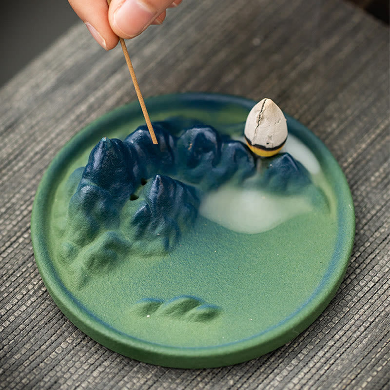 Ceramic Backflow Incense Burner – Hand placing stick incense in blue-green mountain on mat, smoke flowing, zen