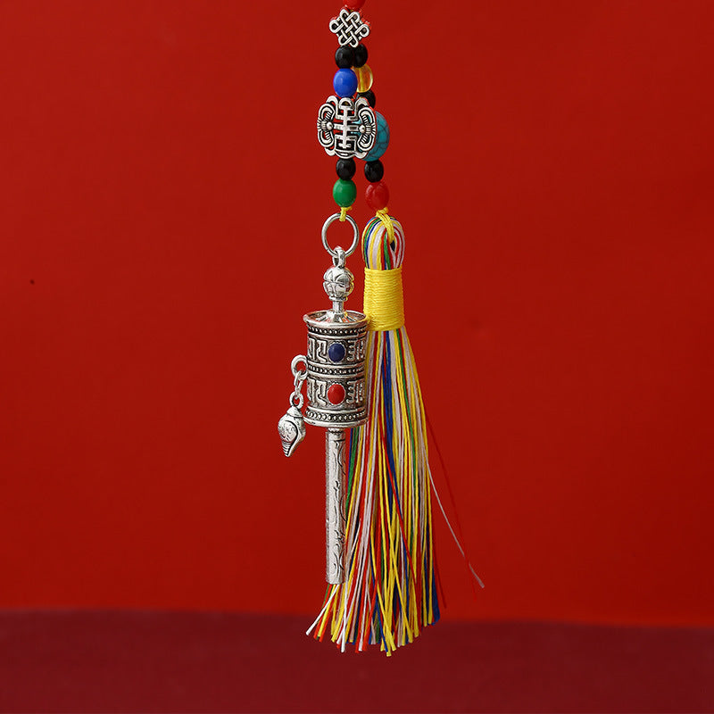 Tibetan Prayer Wheel Keychain – silver-tone prayer wheel pendant with colorful silk tassel and turquoise beads, red background, front view cropped top