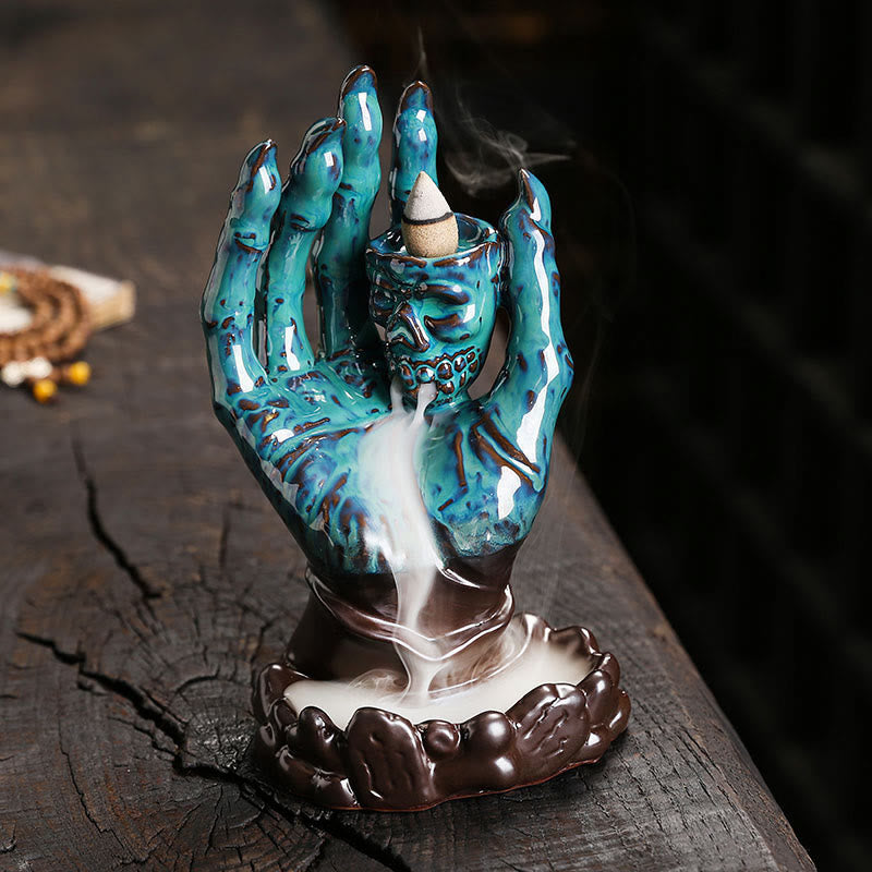 Ceramic Ghost Hand Skull Incense Burner – Turquoise glazed hand with skull cup, backflow smoke pooling in lotus base, dark wood