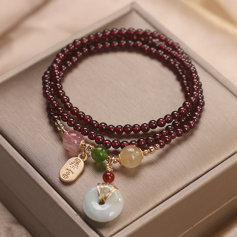 Garnet triple-wrap bracelet with zhao cai wealth-attracting gold tag and white jade ping an kou peace disc pendant with mixed gemstone accent beads on taupe satin display surface