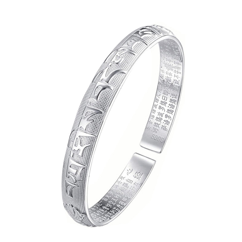 Tibetan silver prayer bangle with raised Tibetan Sanskrit mantra exterior, polished silver finish, adjustable open cuff design on dark surface.