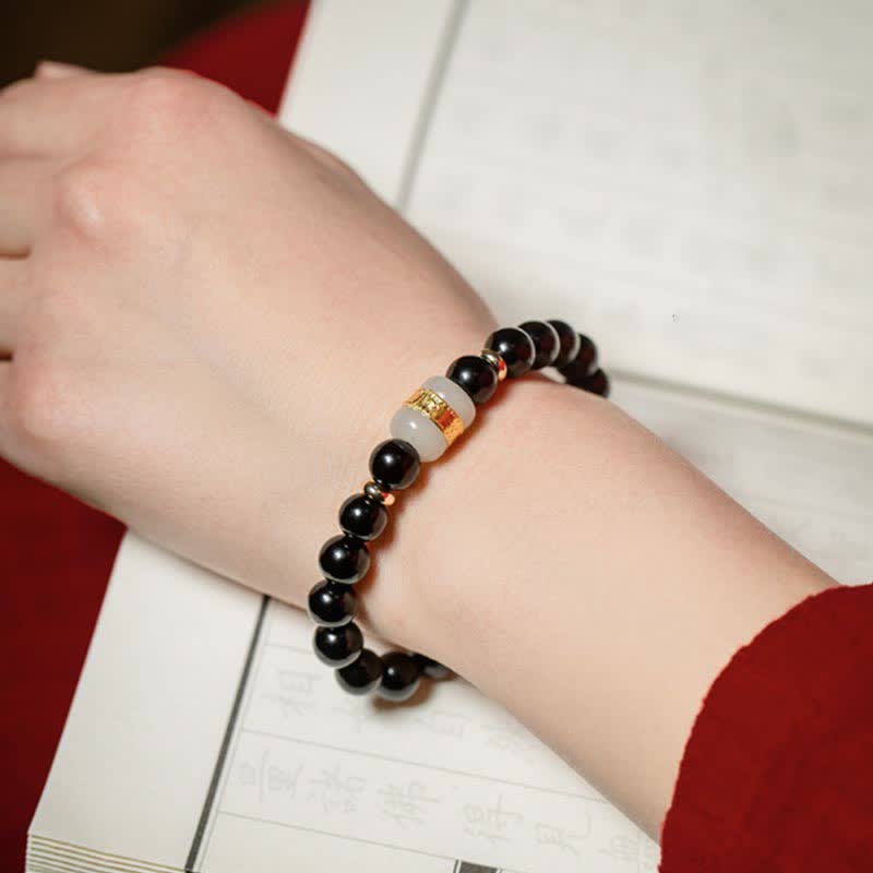 Black Obsidian Jade Bracelet – Worn on wrist with traditional book and red fabric backdrop, lifestyle shot