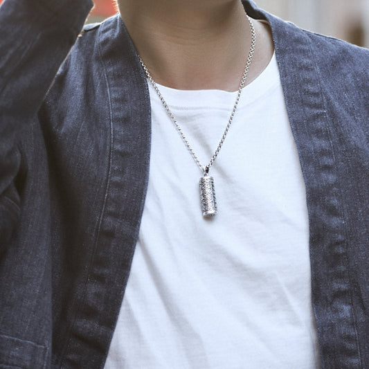 Om Mani Padme Hum Silver Protection Necklace – Silver ball chain necklace with cylindrical prayer wheel pendant worn on model in white t-shirt and dark denim jacket