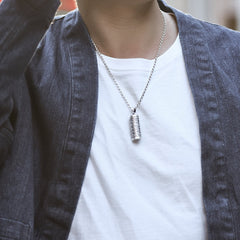 Om Mani Padme Hum Silver Protection Necklace – Silver ball chain necklace with cylindrical prayer wheel pendant worn on model in white t-shirt and dark denim jacket