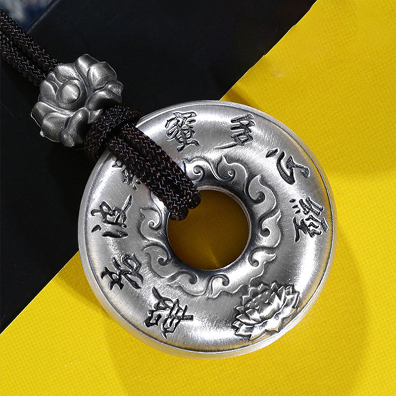 Silver Heart Sutra Pendant – round silver amulet with sutra text and lotus, black cord, yellow-black backdrop
