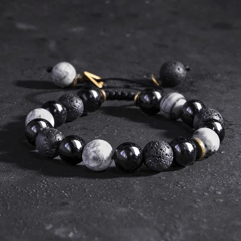 Black Obsidian Lava Rock Yin Yang Bracelet - three-quarter elevated angle on dark textured surface, gold spacer beads