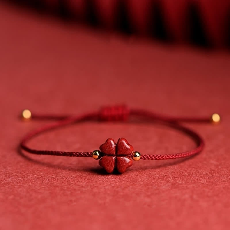 Red cord bracelet with natural cinnabar four leaf clover carved bead gold-toned spacer beads and adjustable sliding knot on matching red textured fabric monochromatic display