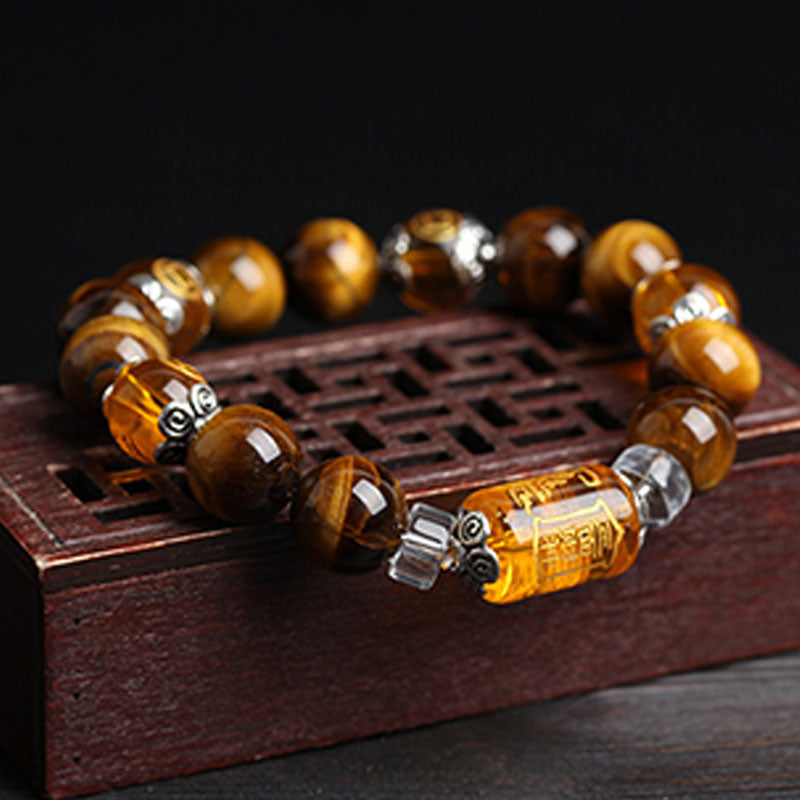 Tiger eye stretch bracelet with carved amber central cylinder bead and silver-toned bead caps displayed on Chinese lattice wooden stand against black background