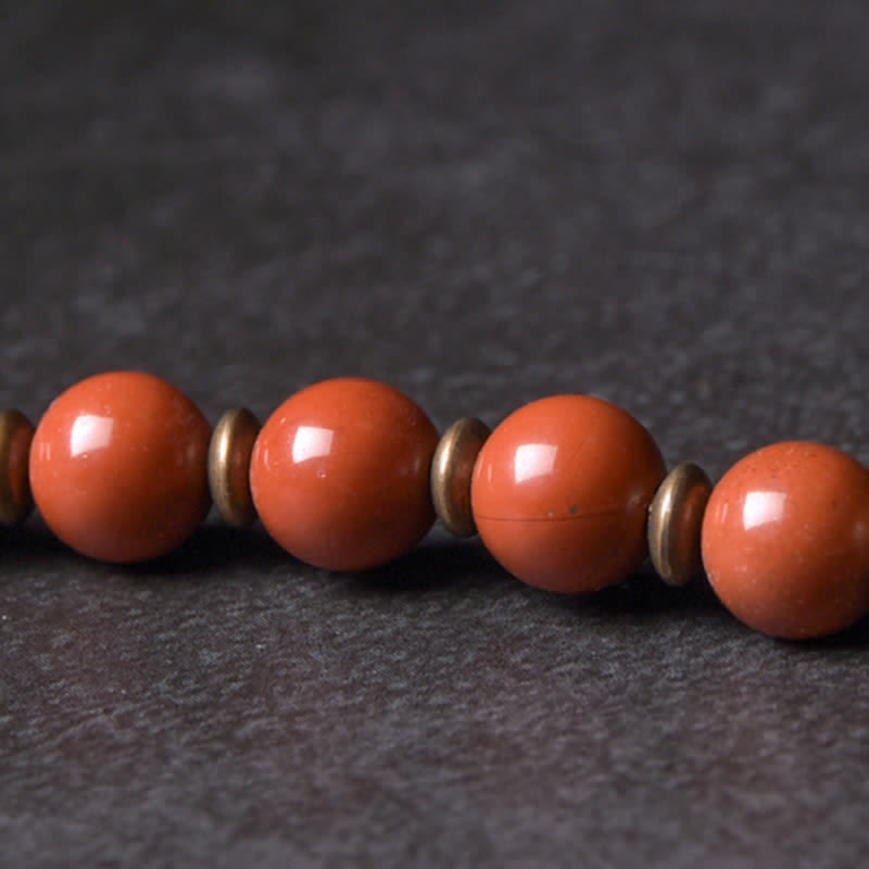 Close-up of red jasper beads with antique brass disc spacers, salmon-orange natural stone beads with aged gold metal accents on dark stone background