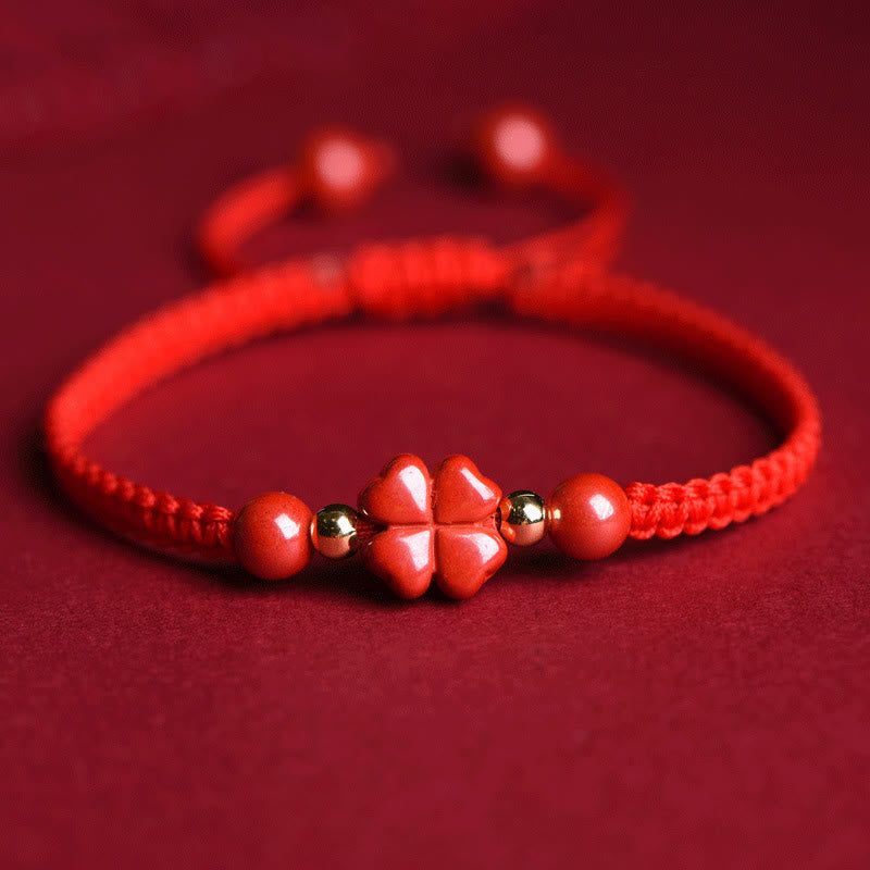 Adjustable red macrame cord bracelet with polished cinnabar four-leaf clover charm, gold accent beads and matching red beads on red background