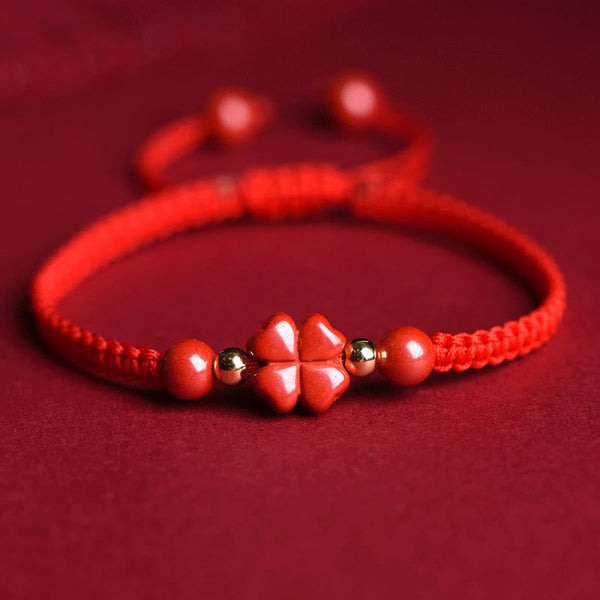 Adjustable red macrame cord bracelet with polished cinnabar four-leaf clover charm, gold accent beads and matching red beads on red background