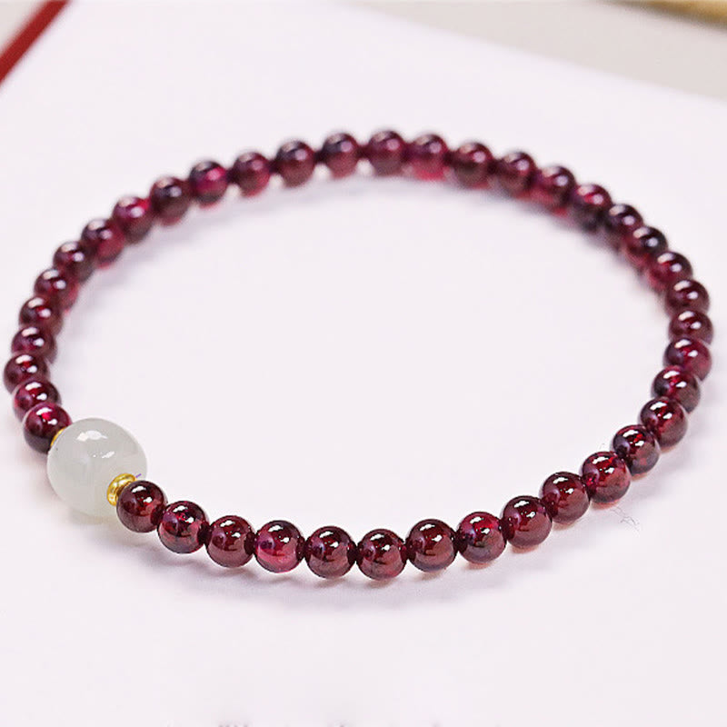 Natural garnet purification bracelet flat lay on pure white background, wine-red beads with central milky jade bead and gold spacer beads, product photography