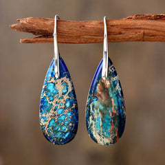 Emperor Stone Healing Crystal Earrings – Teardrop natural stone earrings with royal blue turquoise-green veins and silver hooks on driftwood prop