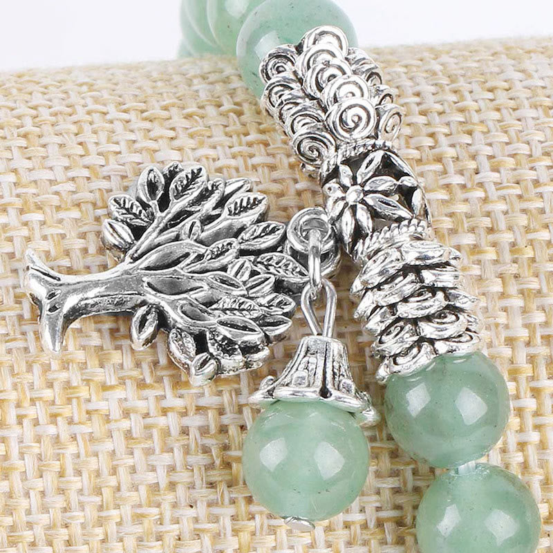 Tree of Life green aventurine bracelet with polished green beads, detailed silver tree pendant with bark texture and leaves, on burlap fabric.