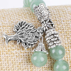 Tree of Life green aventurine bracelet with polished green beads, detailed silver tree pendant with bark texture and leaves, on burlap fabric.