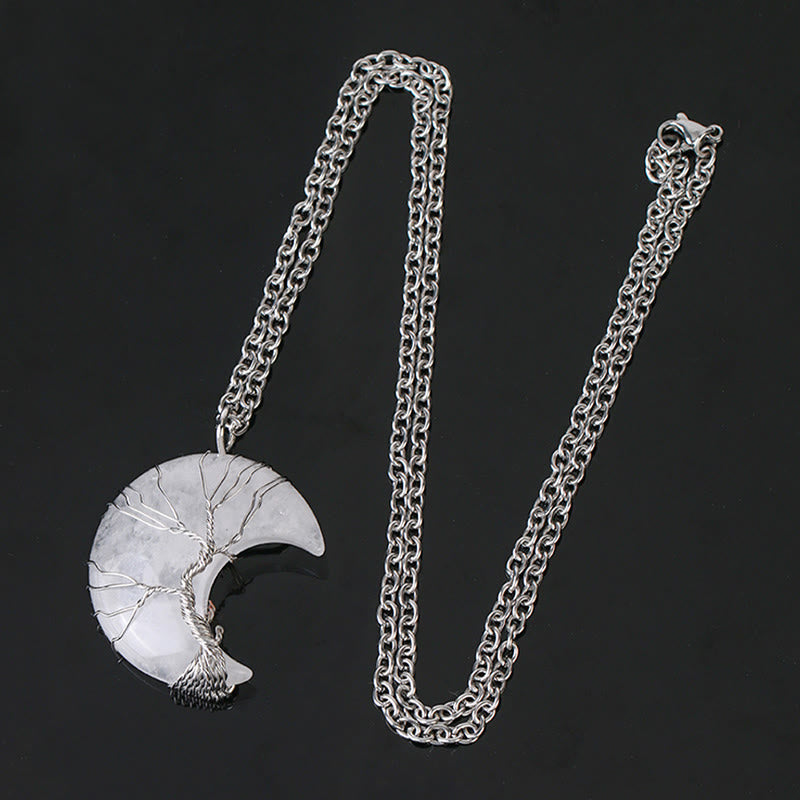 Quartz Crystal Moon Tree of Life Pendant – clear quartz crescent on black background with chain and clasp, flat lay view