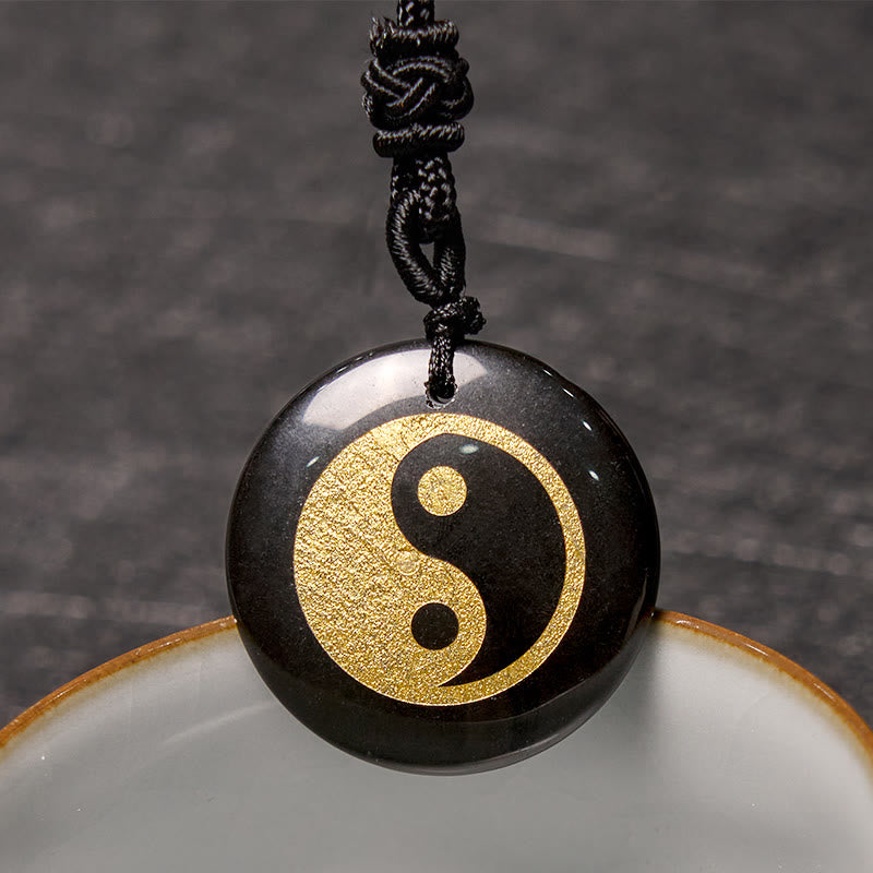 Yin Yang Crystal Necklace – Black obsidian round pendant with gold yin-yang engraving, glossy polished stone on black braided