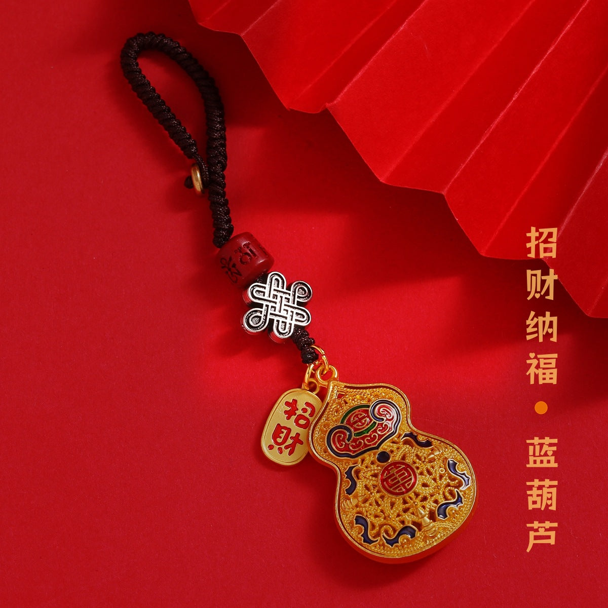 Gold enamel calabash keychain with Chinese knot and peace talisman detail on red background