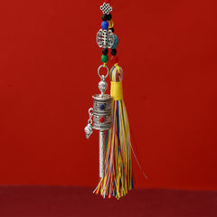 Tibetan Prayer Wheel Keychain – silver-tone prayer wheel pendant with colorful silk tassel and turquoise beads, red background, front view cropped top